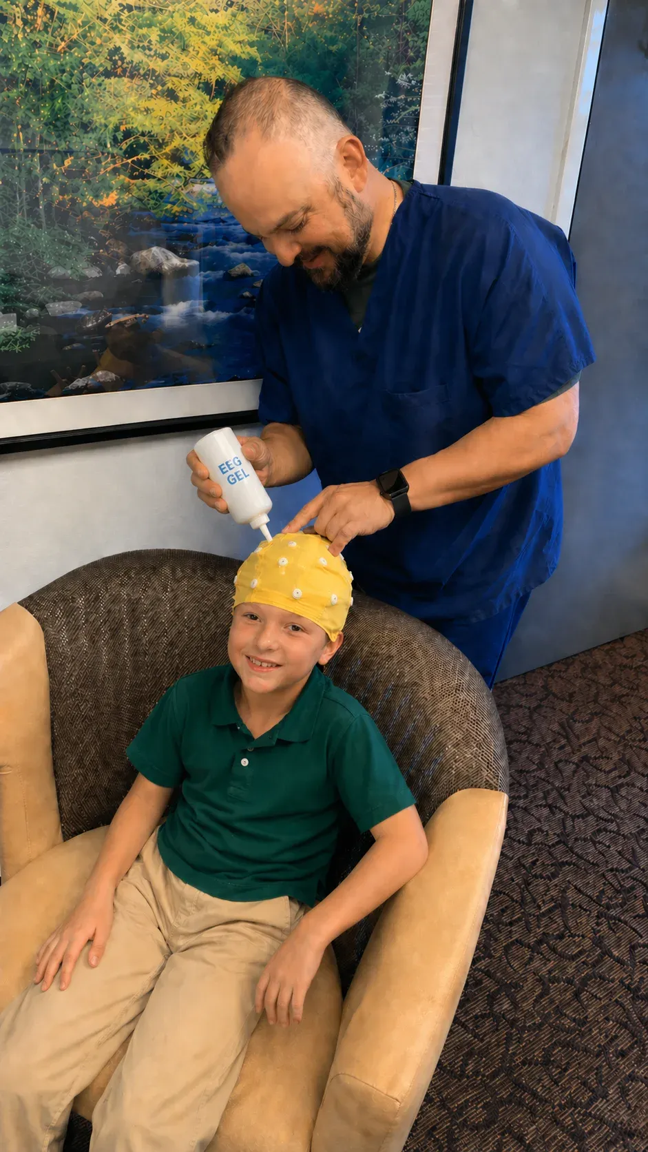 Adrian Quevedo applies EEG gel to a smiling boy’s sensor cap during a brain map at Kerov Health