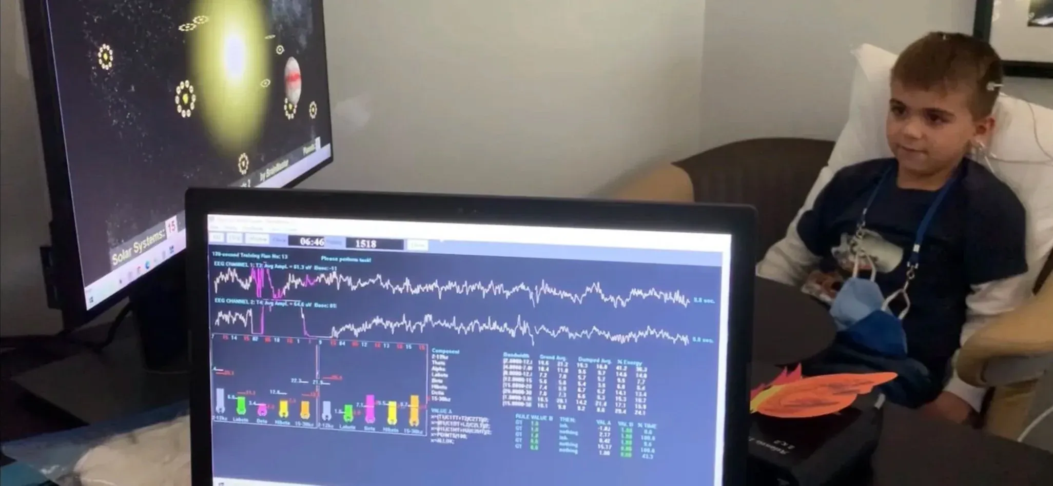 A boy relaxes in a chair during a neurofeedback session while his live brainwave data displays on a monitor